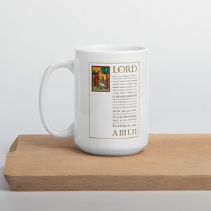 May include: White ceramic mug with a handle, featuring a religious text and illustration. The text includes the word "LORD" at the top and "AMEN" at the bottom. The mug has a gold border around the text and illustration.