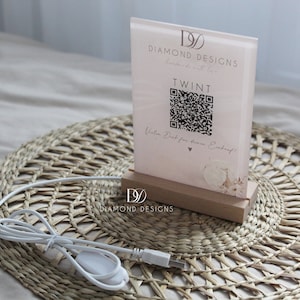 Puede incluir: Un letrero de acrílico rosa con un código QR y el texto "TWINT" y "Vielen Dank für ihren Einkauf!"  El letrero está iluminado y tiene una base de madera con el logotipo "DIAMOND DESIGNS".