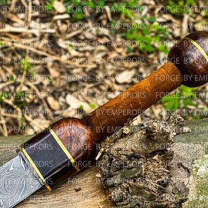 May include: A close-up of a dagger with a wood and metal handle. The handle is wrapped in brown leather and has a gold band around it. The blade is made of Damascus steel and has a wavy pattern.
