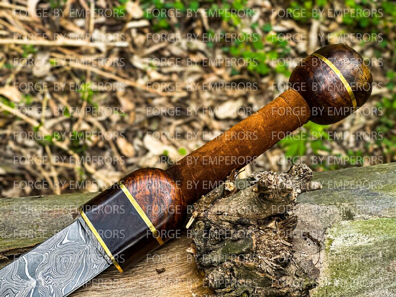 May include: A close-up of a dagger with a wood and metal handle. The handle is wrapped in brown leather and has a gold band around it. The blade is made of Damascus steel and has a wavy pattern.