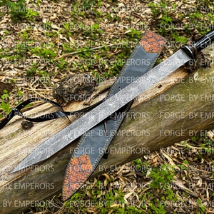 May include: A long, silver sword with a black handle and a leather scabbard. The sword has a decorative pattern on the blade and is resting on a wooden log. The scabbard has a brown leather strap with a buckle.