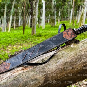 May include: A black leather scabbard with a brown snakeskin pattern and a strap. The scabbard is resting on a tree trunk in a forest setting.