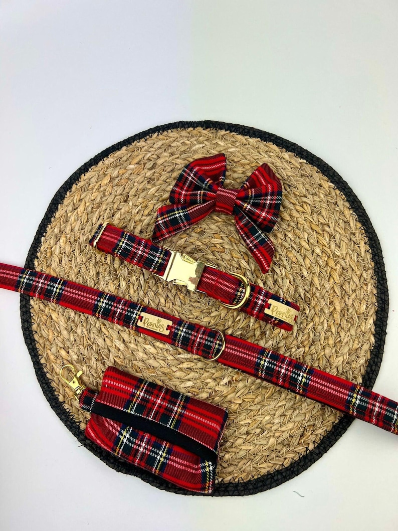 May include: A red and black plaid dog collar, leash, bow tie, and waste bag holder set. The collar and leash have gold-colored hardware. The bow tie is a matching plaid pattern. The waste bag holder is rectangular with a black elastic band.