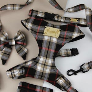 May include: A dog harness, lead, collar, and bow tie set in a black, tan, and red plaid pattern. The harness has a wooden tag that says "Peonies". The lead has a black metal clasp.