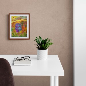 May include: A framed painting depicting two figures in a desert landscape with a yellow sun and cacti. The figures are wearing purple and blue clothing. The painting is on a white desk with a potted plant and glasses.