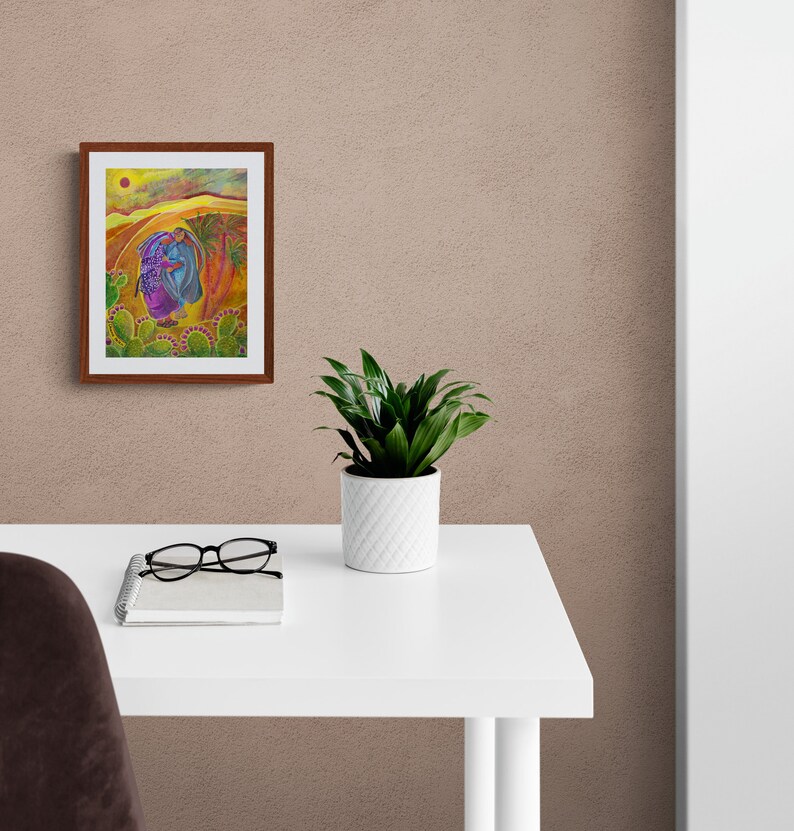 May include: A framed painting depicting two figures in a desert landscape with a yellow sun and cacti. The figures are wearing purple and blue clothing. The painting is on a white desk with a potted plant and glasses.