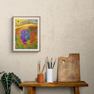 May include: A framed painting depicting two figures walking through a desert landscape. The figures are wearing colourful clothing and carrying a basket of purple fruit. The background is a yellow and orange desert with a bright orange sun in the sky.