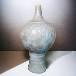 May include: A ceramic vase with a light blue and white glaze. The vase has a round body and a wide base.