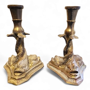 May include: A pair of antique brass candle holders featuring a design of three fish on the base. The candle holders are in good condition with some signs of age and wear.