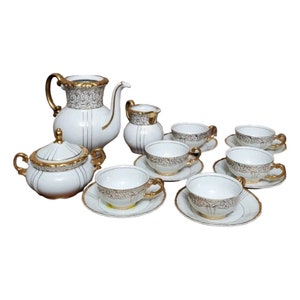 May include: A white porcelain tea set with gold accents. The set includes a teapot, creamer, sugar bowl, and six cups and saucers.