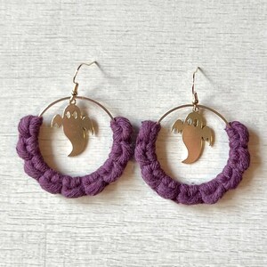 May include: Purple crocheted hoop earrings with a gold ghost charm hanging from each hoop.