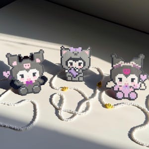 May include: Three pixel art figures crafted from fused beads, each depicting a character in a different costume. The figures are arranged in a row, connected by a long string of small white beads interspersed with yellow smiley face beads.