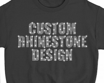 Op de afbeelding: Zwart sweatshirt met de woorden "CUSTOM RHINESTONE DESIGN" in witte strass steentjes.