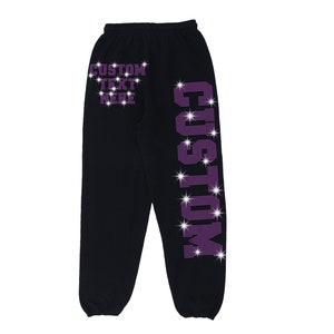 K&ouml;nnte beinhalten: Schwarze Jogginghose mit einem violetten Strass-Design, das "CUSTOM" auf dem rechten Bein und "CUSTOM TEXT HERE" auf dem linken Bein tr&auml;gt.
