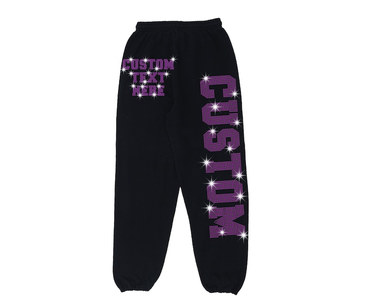 K&ouml;nnte beinhalten: Schwarze Jogginghose mit einem violetten Strass-Design, das "CUSTOM" auf dem rechten Bein und "CUSTOM TEXT HERE" auf dem linken Bein tr&auml;gt.