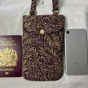 May include: A small, brown and gold patterned crossbody phone bag with a silver button closure. The bag is shown next to a passport and a silver iPhone.