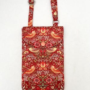 May include: A red crossbody bag with a floral and bird pattern. The bag has a long adjustable strap and a flap closure with a button.