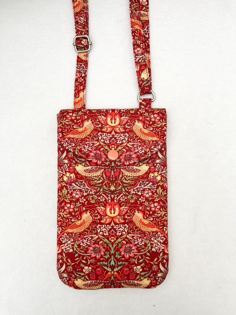 May include: A red crossbody bag with a floral and bird pattern. The bag has a long adjustable strap and a flap closure with a button.