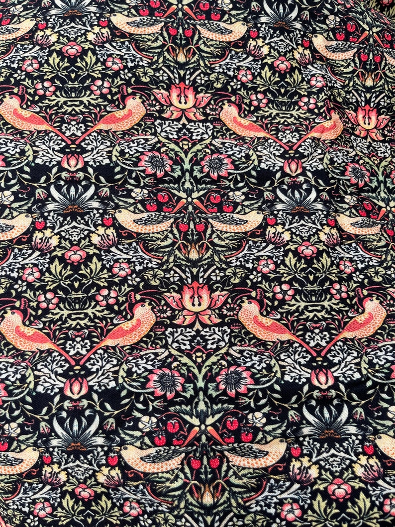 May include: A black fabric with a repeating pattern of stylized birds, flowers, and leaves. The pattern is in shades of pink, green, and white.