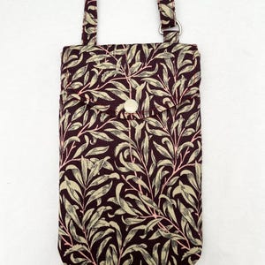 May include: A small burgundy fabric phone pouch with a leafy pattern and a white button closure. The pouch has a long adjustable strap.
