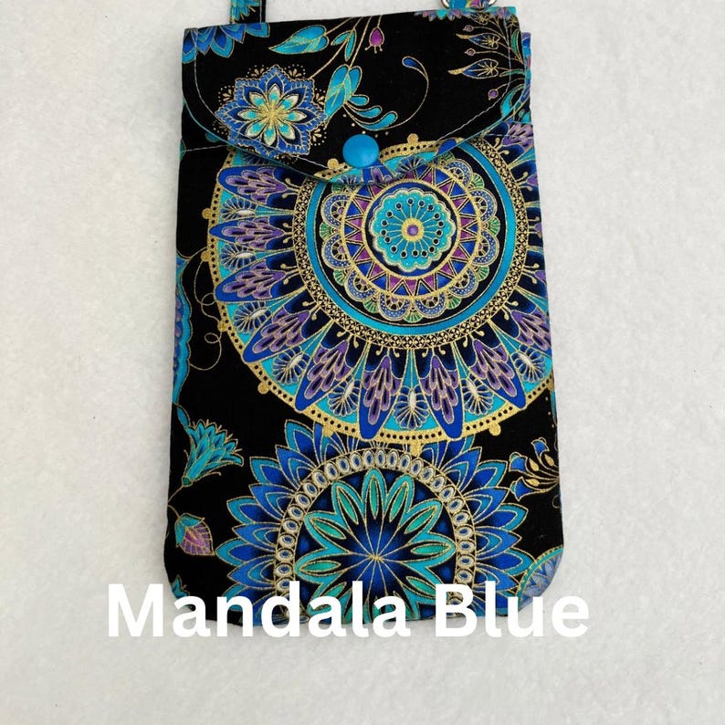 May include: A black phone case with a flap and a blue button closure. The case is decorated with a mandala pattern in shades of blue, teal, and gold. The text "Mandala Blue" is printed at the bottom.