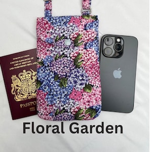 May include: A floral print phone crossbody bag with a matching strap. The bag features a button closure and a design of pink, purple, and blue flowers. A black smartphone and a passport are next to the bag. The text "Floral Garden" is at the bottom.