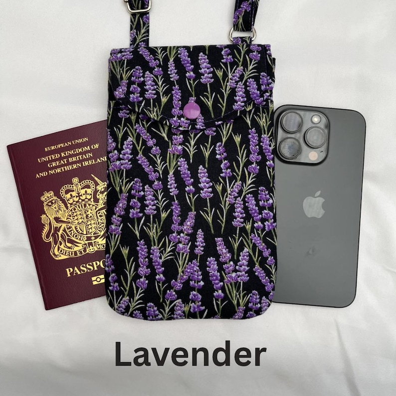 Puede incluir: Un bolso bandolera negro para tel&eacute;fono con un estampado floral de lavanda, un bot&oacute;n morado y correas ajustables. La palabra "Lavender" est&aacute; impresa en la parte inferior. Un pasaporte y un smartphone est&aacute;n al lado del bolso.