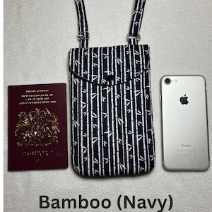 May include: Navy blue and white bamboo print crossbody phone bag with adjustable straps. The bag has a flap closure with a black button. A passport and a smartphone are next to the bag. The text "Bamboo (Navy)" is at the bottom.