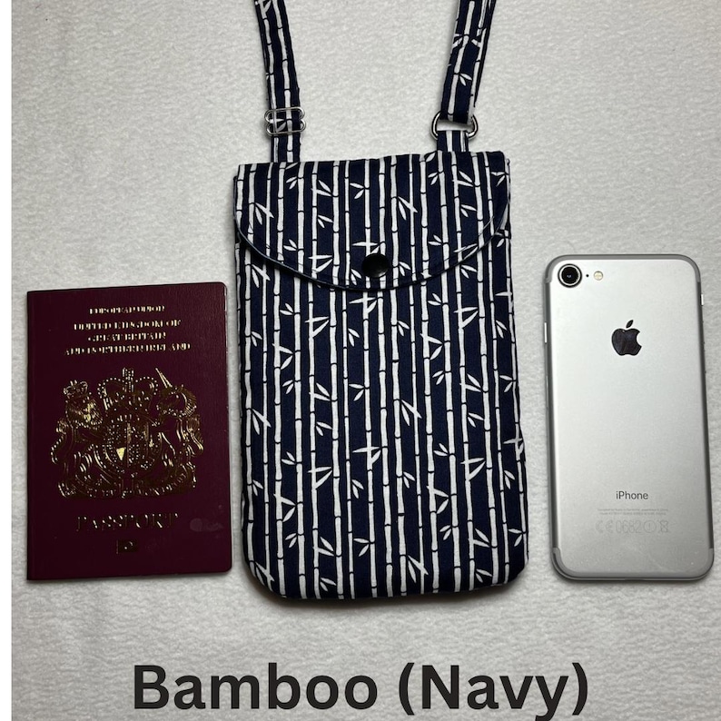 May include: Navy blue and white bamboo print crossbody phone bag with adjustable straps. The bag has a flap closure with a black button. A passport and a smartphone are next to the bag. The text "Bamboo (Navy)" is at the bottom.