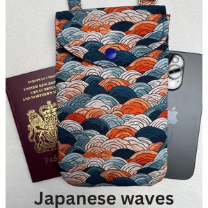 May include: A fabric phone crossbody bag with a Japanese wave pattern in shades of blue, orange, and white. The bag has a flap closure with a blue button and a strap. A passport and a smartphone are next to the bag. The text "Japanese waves" is at the bottom.