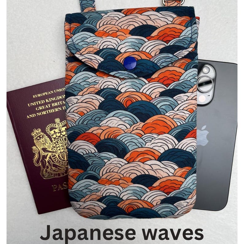 May include: A fabric phone crossbody bag with a Japanese wave pattern in shades of blue, orange, and white. The bag has a flap closure with a blue button and a strap. A passport and a smartphone are next to the bag. The text "Japanese waves" is at the bottom.