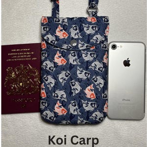 May include: A navy blue phone bag with a flap closure, featuring a pattern of white and orange koi fish. The bag has adjustable straps and a silver snap closure. The text "Koi Carp" is at the bottom of the image.