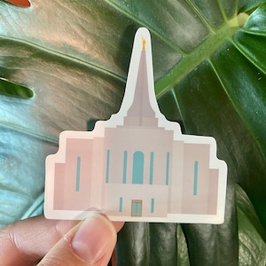 Puede incluir: Una pegatina de un templo rosa y blanco con una estatua dorada en la parte superior. El templo tiene ventanas azules y una puerta marrón.