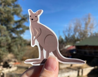 May include: A brown kangaroo sticker with a white outline. The kangaroo is standing on its hind legs with its tail curled behind it.