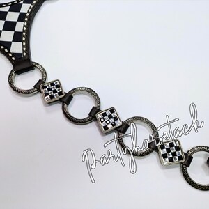 May include: A black and white checkered pattern belt with silver-tone rings and square accents. The belt has a leather strap and a decorative design. The text "Partyhorsetack" is visible.