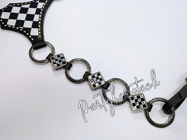 May include: A black and white checkered pattern belt with silver-tone rings and square accents. The belt has a leather strap and a decorative design. The text "Partyhorsetack" is visible.