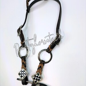 May include: A brown and black leather horse bridle with a braided browband and cheekpieces. The bridle features silver-toned metal rings and decorative diamond-shaped accents with a black and white checkered pattern. The text "Partyhorsetack" is written in cursive.