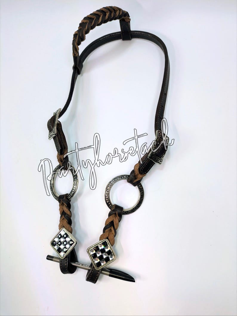 May include: A brown and black leather horse bridle with a braided browband and cheekpieces. The bridle features silver-toned metal rings and decorative diamond-shaped accents with a black and white checkered pattern. The text "Partyhorsetack" is written in cursive.