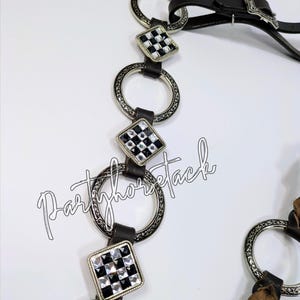 May include: A close-up of a horse bridle with a black leather strap and silver-colored metal accents. The bridle features decorative square accents with a black and white checkered pattern. The text "Partyhorsetack" is visible.