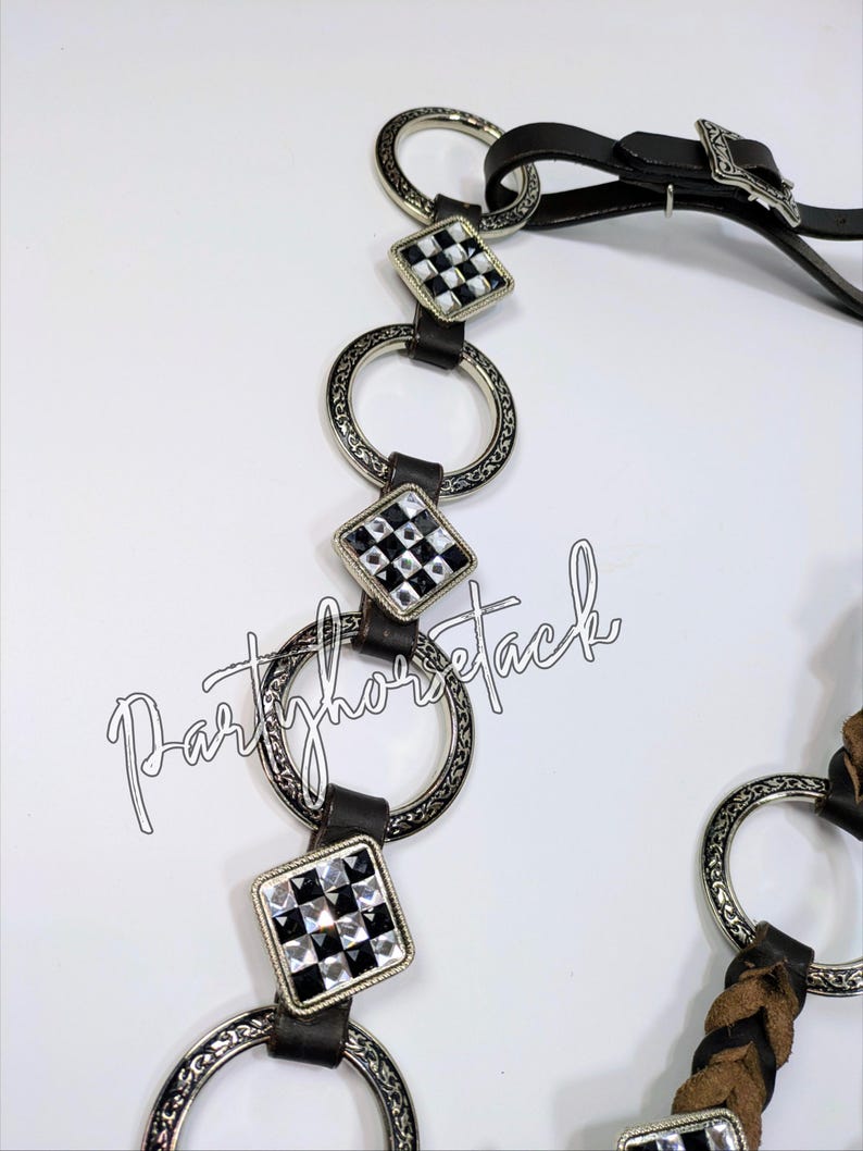 May include: A close-up of a horse bridle with a black leather strap and silver-colored metal accents. The bridle features decorative square accents with a black and white checkered pattern. The text "Partyhorsetack" is visible.