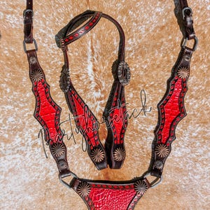 May include: A western-style horse bridle set with a red and brown design. The set includes a headstall, browband, and breast collar. The red sections have a textured pattern, and the set is decorated with silver-colored conchos.