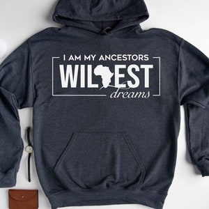 May include: Dark heather grey hoodie with a white graphic print that says "I am my ancestors wildest dreams" with an outline of the continent of Africa.