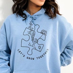May include: Light blue hoodie with a black graphic of a puzzle piece with flowers and the text "Let's Grow Together".