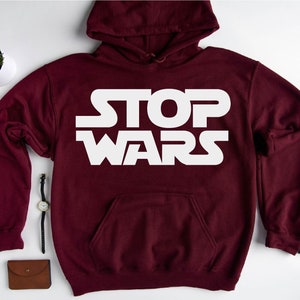 May include: Maroon hoodie with a white graphic that says "STOP WARS" in a stylised font.