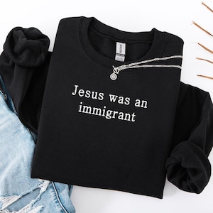 May include: Black sweatshirt with the text "Jesus was an immigrant" in white lettering.
