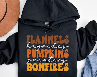 May include: Black hooded sweatshirt with the text "FLANNELS hayrides PUMPKINS sweaters BONFIRES" in orange, brown, and yellow lettering.