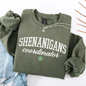 May include: A green sweatshirt with the text "SHENANIGANS coordinator" in white lettering and a green four-leaf clover graphic.