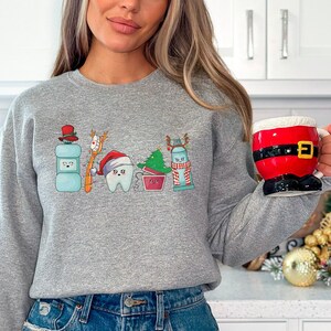以下が含まれることがあります： サンタの帽子をかぶった歯、歯磨き粉、フロス、歯ブラシ、クリスマスツリーが描かれたグレーのトレーナーです。