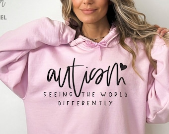 May include: Pink hooded sweatshirt with the text "autism" and a heart symbol. The text below says "seeing the world differently".