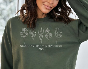 以下が含まれることがあります： 「Neurodiversity is beautiful」というテキストとスタイリッシュな無限大記号が書かれた緑色のスウェットシャツ。スウェットシャツには白い花の列が描かれています。